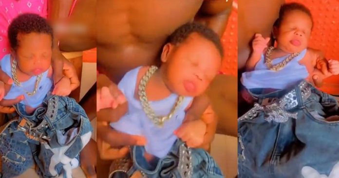 Outrage Online As Video Shows Man Dressing Infant Son In Oversized Clothing And Heavy Jewelry (WATCH)